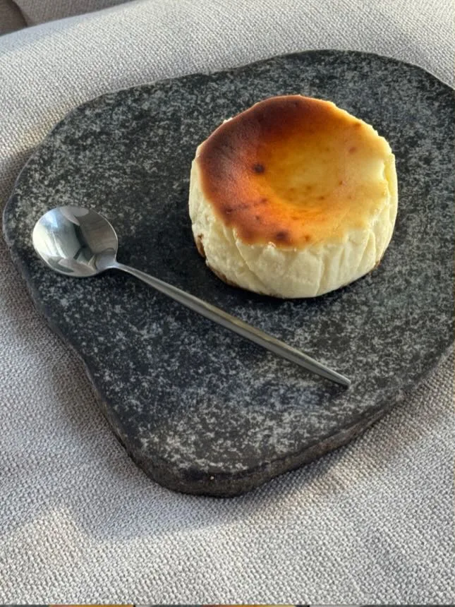 A Classic tartza on a dark basalt slab, scorched golden top, a silver spoon beside it.